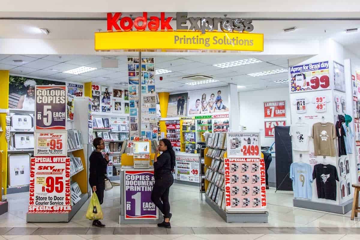 Een Kodak Express-winkel met printdiensten in een winkelcentrum, met displays voor fotoprints, documenten en accessoires, en klanten die bij de toonbank staan.